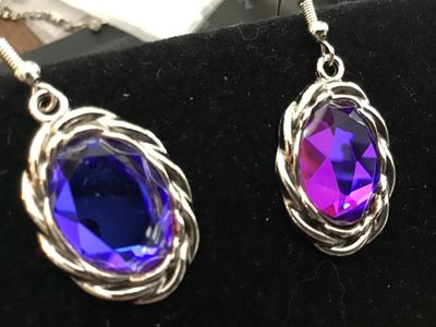Sale Photo Thumbnail #163: Pair of silver-tone drop hook earrings featuring oval-cut faceted purple glass or rhinestone stones framed in a twisted rope border. Overall length is approximately 1.5 inches including hook wires. Good condition with light wear.