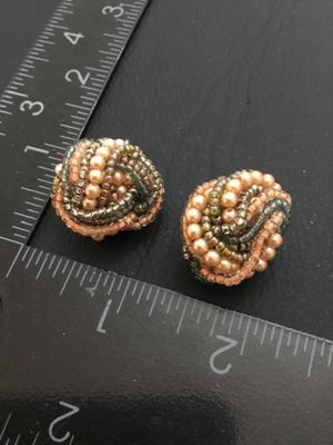 Sale Photo Thumbnail #161: Pair of vintage clip-on cluster earrings featuring woven seed beads and faux pearls in shades of peach, grey, and metallic tones on gold-tone backing plates. Each earring measures approximately 1 inch in diameter. In good vintage condition with secure cli