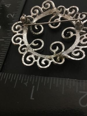 Sale Photo Thumbnail #27: Vintage Sarah Coventry silver-tone brooch featuring an intricate openwork scrollwork design. Marked © SARAH COV on the back. Measures approximately 1.75 inches in diameter. Features a functional rollover safety clasp. Good vintage condition with light we