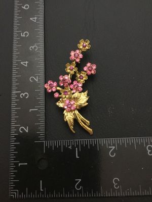 Sale Photo Thumbnail #57: A vintage gold-tone floral bouquet brooch signed RMN, featuring textured leaves and flowers set with sparkling pink rhinestones. Includes a rollover safety clasp on the back. Measures approximately 2.5 inches in length.