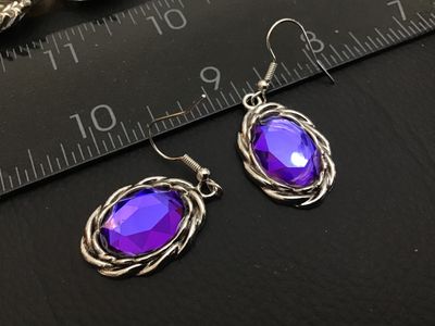 Sale Photo Thumbnail #165: Pair of silver-tone drop hook earrings featuring oval-cut faceted purple glass or rhinestone stones framed in a twisted rope border. Overall length is approximately 1.5 inches including hook wires. Good condition with light wear.