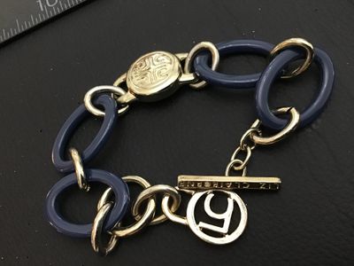 Sale Photo Thumbnail #154: A Liz Claiborne costume jewelry chain bracelet featuring bold blue resin oval links intertwined with gold-tone metal links, a central round engraved medallion, and a branded toggle clasp with an 'LC' charm. In good pre-owned condition with light surface w