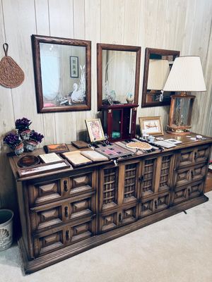 Large vintage Mediterranean-style wooden credenza with matching framed wall mirrors, topped with a table lamp, framed art, and various...