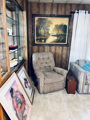 Vintage tufted fabric recliner armchair set against wood-paneled walls, with a framed landscape painting, vintage suitcase, and framed...
