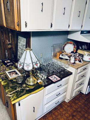 Vintage Tiffany-style stained glass table lamp alongside various glassware collections, framed artwork, and kitchen collectibles arranged...