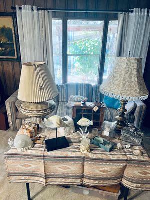 A table display of vintage home decor featuring two large table lamps, various seashell accents, small wooden collectibles, and a...