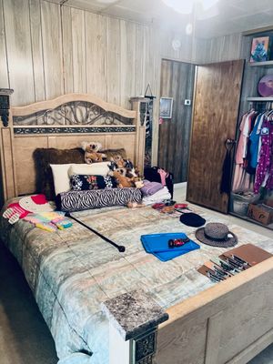 Light wood Queen bed set with ornate headboard, displayed with stuffed koalas, decorative pillows, hats, and assorted household items.