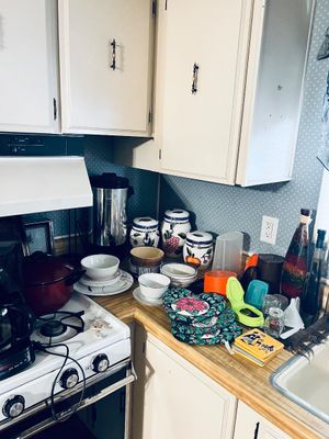 Assorted kitchenware and small appliances display, including a coffee urn, ceramic canisters, pot holders, and stacked dishes set on a...