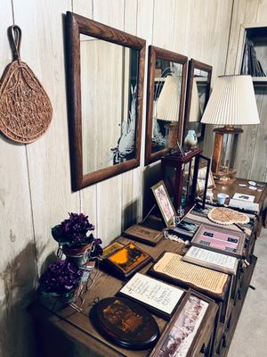 Collection of home decor items arranged on a long wooden dresser, including framed wall mirrors with etched glass designs, framed...