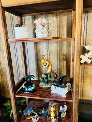Rustic wooden shelving unit displaying various decorative items, including a Kokopelli figure, ceramic swan, decorative pitcher, and...