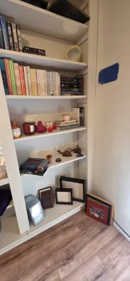 Sale Photo Thumbnail #29: White built-in bookcase filled with hardback and paperback books, decorative candles, small knick-knacks, and various picture frames.
