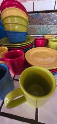 Sale Photo Thumbnail #23: Collection of colorful ceramic dinnerware, including Fiesta-style ridged mugs, bowls, and plates in red, yellow, green, and blue.