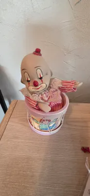 Sale Photo Thumbnail #16: Vintage musical clown figurine emerging from a drum base, featuring a porcelain-style head with painted facial details, lace collar, and striped fabric outfit.