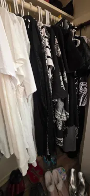 Sale Photo Thumbnail #38: Closet filled with women's clothing on hangers, primarily in black and white styles, with various pairs of shoes arranged below.