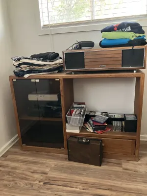 Sale Photo Thumbnail #47: Vintage oak media console cabinet featuring dark glass door, filled with folded clothing, CDs, media accessories, and a vintage tabletop stereo system on top.