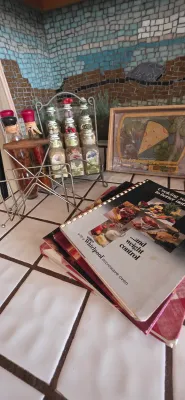 Sale Photo Thumbnail #21: Collection of vintage kitchen accessories, including a Whirlpool microwave cookbook, a wire spice rack with glass jars, decorative oil bottles, and framed art.