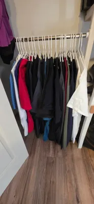 Sale Photo Thumbnail #32: Collection of men's short-sleeve shirts and t-shirts hanging on white plastic hangers inside a closet.