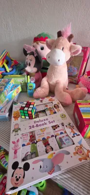 Sale Photo Thumbnail #10: Collection of children's toys and books, including a Disney Baby Deluxe 24-Book Set, plush giraffe, Minnie Mouse doll, Rubik's cube, and boxed puzzles.