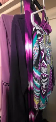 Sale Photo Thumbnail #40: Collection of women's purple and patterned garments hanging on plastic hangers in a closet.