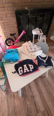 Sale Photo Thumbnail #7: Collection of children's items including folded clothing on a white play table, a pink Strider balance bike, and a toy piano.