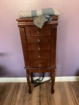 Sale Photo Thumbnail #44: Traditional wooden standing jewelry armoire with multiple drawers and side doors, topped with folded scarves and neckties.
