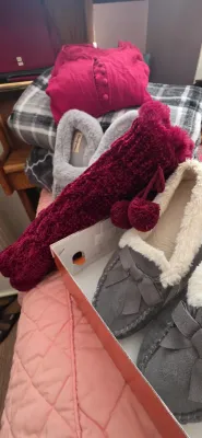 Sale Photo Thumbnail #37: Collection of cozy winter apparel including grey plush-lined moccasin slippers, fuzzy slippers, maroon knit socks with pom-poms, a magenta top, and folded plaid blankets.