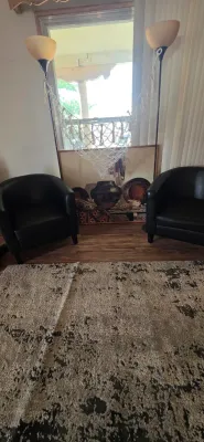Sale Photo Thumbnail #14: Pair of modern black leatherette barrel chairs flanked by matching torchiere floor lamps, set over a textured area rug.