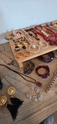Sale Photo Thumbnail #15: Collection of vintage costume jewelry, including beaded necklaces, gold-tone door-knocker earrings, pearl hoop earrings, and black tassel drop earrings arranged on a wooden riser and tabletop.
