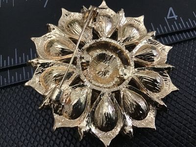 Sale Photo Thumbnail #32: Vintage gold-tone layered flower brooch featuring pale pink pear-cut rhinestones, dark pink round accent rhinestones, white enamel details, and a central iridescent aurora borealis rhinestone. Measures approximately 2 inches in diameter. Pin back with C-c