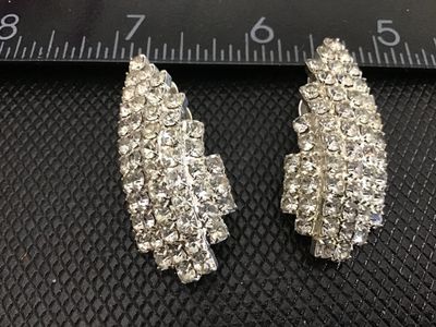 Sale Photo Thumbnail #206: Pair of vintage silver-tone clip-on earrings set with sparkling multi-tiered clear rhinestones. Curved leaf or wing-style design. Each earring measures approximately 1.5 inches long. Clip backs are in functional condition with bright, clear stones.
