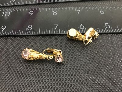 Sale Photo Thumbnail #156: Pair of vintage gold-tone clip-on earrings featuring filigree cone drops set with light purple or amethyst-colored round rhinestones. Each earring has a smaller rhinestone set at the clip base with a dangling filigree component below. Measure approximatel