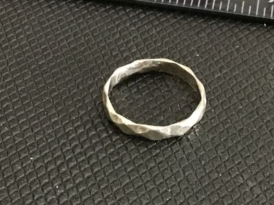 Sale Photo Thumbnail #220: A silver-tone metal ring featuring a geometric, faceted/hammered exterior texture. Ring size measures approximately 6.75 on a ring sizer mandrel. Item shows slight surface wear consistent with age and use.