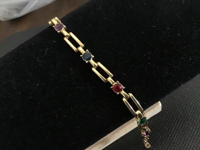 Sale Photo Thumbnail #215: A vintage gold-tone open bar-link bracelet featuring round, bezel-set multi-colored rhinestones in red, green, blue, and purple. Measures approximately 7 inches in length and features a fold-over clasp closure. Shows light signs of wear consistent with ag