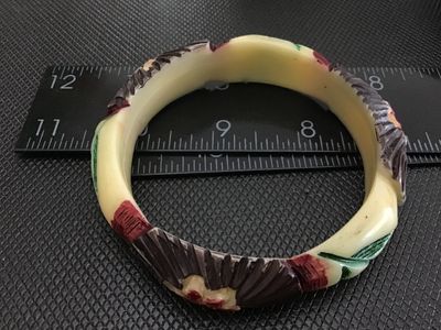 Sale Photo Thumbnail #57: Vintage carved Celluloid bangle bracelet featuring painted floral and fan details in red, green, brown, and cream tones. Measures approximately 3 inches in outer diameter. Shows minor surface wear consistent with age.