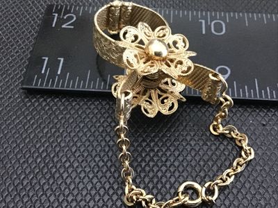 Sale Photo Thumbnail #47: Vintage gold-tone metal glove clip featuring a delicate filigree flower center design, textured metal band clip, and an attached safety chain with spring ring clasp. Decorative antique/vintage fashion accessory. Measures approximately 3 to 4 inches in len