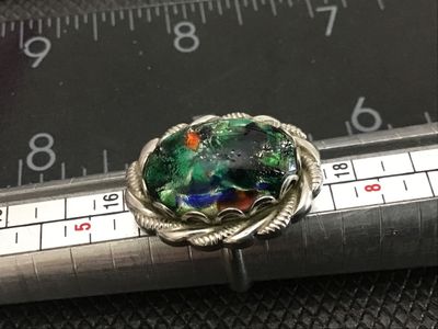 Sale Photo Thumbnail #141: Vintage statement ring featuring an oval green, black, and multicolor art glass cabochon set in a scalloped, rope-twist silver tone bezel. The ring has an adjustable band as shown in the photos. Measures approximately size 8 to 9 as shown on the ring size