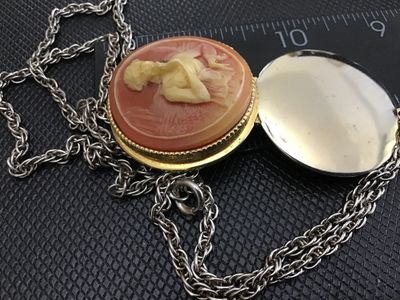 Sale Photo Thumbnail #40: Vintage costume jewelry necklace featuring a round hinged locket with a faux cameo motif depicting a classic female profile against a peachy-pink background set in a gold-tone beaded bezel. Attached to a silver-tone/gold-tone chain. The pendant measures a
