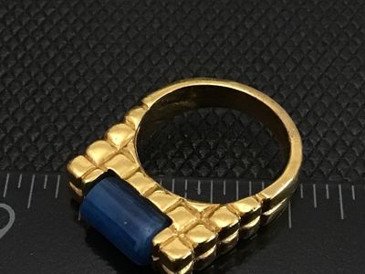 Sale Photo Thumbnail #14: Gold-tone fashion statement ring featuring a textured waffle/grid band design set with a cylindrical blue stone resembling lapis lazuli or sodalite. Ring measures approximately size 7.5 on a ring mandrel. Good pre-owned condition with light surface wear v