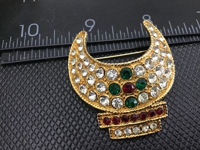 Sale Photo Thumbnail #37: Vintage gold-tone crescent moon shaped brooch set with clear, green, and red rhinestones. Features a textured finish and a standard pin back fastener. Measures approximately 1.5 inches in length. In good vintage condition with all stones intact.