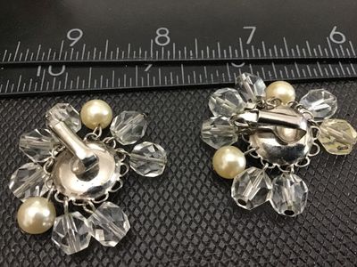 Sale Photo Thumbnail #25: Pair of vintage clip-on cluster earrings featuring central faux pearl cabochons framed by silver-tone filigree metalwork, surrounded by dangling faceted clear crystal beads and smaller accent faux pearls. Measure approximately 1.25 inches across. Shows mi