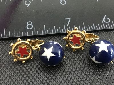Sale Photo Thumbnail #139: Pair of gold-tone clip-on earrings featuring a nautical ship's wheel with red enamel star accents, dangling blue beads decorated with white stars. Patriotic red, white, and blue motif. Good vintage condition with light wear on metal finish.
