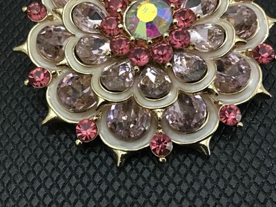 Sale Photo Thumbnail #33: Vintage gold-tone layered flower brooch featuring pale pink pear-cut rhinestones, dark pink round accent rhinestones, white enamel details, and a central iridescent aurora borealis rhinestone. Measures approximately 2 inches in diameter. Pin back with C-c
