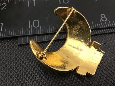 Sale Photo Thumbnail #38: Vintage gold-tone crescent moon shaped brooch set with clear, green, and red rhinestones. Features a textured finish and a standard pin back fastener. Measures approximately 1.5 inches in length. In good vintage condition with all stones intact.