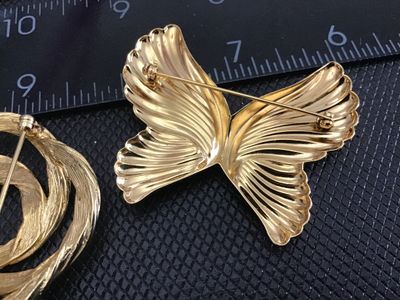 Sale Photo Thumbnail #162: Pair of vintage gold-tone brooches featuring a textured swirl knot brooch signed Monet and a ribbed butterfly brooch. Both pieces feature secure pin backs and classic mid-to-late 20th century styling. In very good vintage condition with bright gold-tone f
