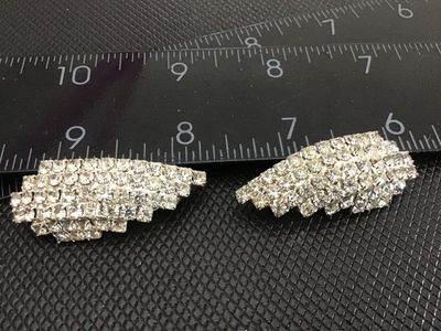 Sale Photo Thumbnail #204: Pair of vintage silver-tone clip-on earrings set with sparkling multi-tiered clear rhinestones. Curved leaf or wing-style design. Each earring measures approximately 1.5 inches long. Clip backs are in functional condition with bright, clear stones.