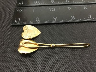 Sale Photo Thumbnail #77: Gold tone bodkin / ribbon threader featuring a hinged, opening heart-shaped locket top. The locket features floral and scroll engraved detailing on the front face. Measures approximately 3 inches in length. In good vintage condition with minor surface wea