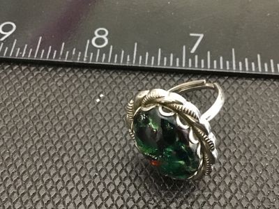 Sale Photo Thumbnail #144: Vintage statement ring featuring an oval green, black, and multicolor art glass cabochon set in a scalloped, rope-twist silver tone bezel. The ring has an adjustable band as shown in the photos. Measures approximately size 8 to 9 as shown on the ring size