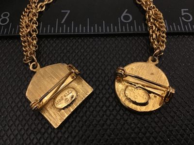 Sale Photo Thumbnail #90: A vintage Anne Klein gold-tone double brooch featuring textured lion head motifs connected by a multi-strand dangled chain. Marked ANNE KLEIN on the back of the shield-shaped pin. Features rollover safety clasp closures. In good vintage condition with lig