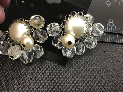 Sale Photo Thumbnail #22: Pair of vintage clip-on cluster earrings featuring central faux pearl cabochons framed by silver-tone filigree metalwork, surrounded by dangling faceted clear crystal beads and smaller accent faux pearls. Measure approximately 1.25 inches across. Shows mi
