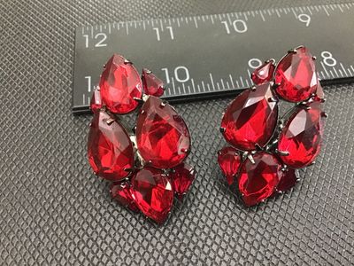 Sale Photo Thumbnail #3: Pair of vintage cluster clip-on earrings featuring multi-faceted, teardrop-cut red rhinestones set in gunmetal tone metal backings. Each earring measures approximately 1.5 inches in length. In good condition with functional clip closures and light surface